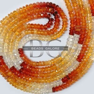 May include: A strand of faceted gemstone beads in shades of orange, yellow, and white. The beads are arranged in a graduated pattern, with the darkest orange beads at the top and the lightest white beads at the bottom. The beads are strung on a clear thread and are ready to be used for jewelry making.