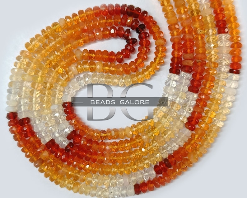 May include: A strand of faceted gemstone beads in shades of orange, yellow, and white. The beads are arranged in a graduated pattern, with the darkest orange beads at the top and the lightest white beads at the bottom. The beads are strung on a clear thread and are ready to be used for jewelry making.