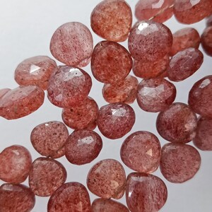 May include: A strand of faceted, translucent, red gemstone beads. The beads are round and have a slightly irregular shape. The beads are strung on a clear thread.