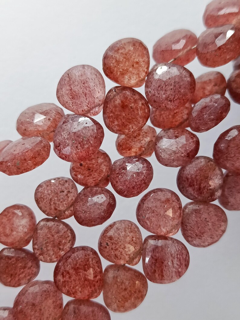 May include: A strand of faceted, translucent, red gemstone beads. The beads are round and have a slightly irregular shape. The beads are strung on a clear thread.