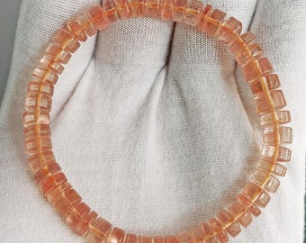 May include: A circular bracelet composed of numerous small, translucent, peach-colored disc-shaped beads. The beads are strung together on a thin, visible cord, creating a uniform, repeating pattern of light orange and pinkish-toned gemstone segments.