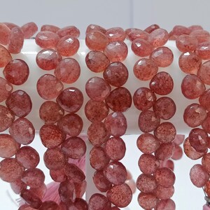 May include: A strand of faceted, reddish-brown gemstone beads. The beads are round and have a slightly irregular shape. They are strung on a clear thread.