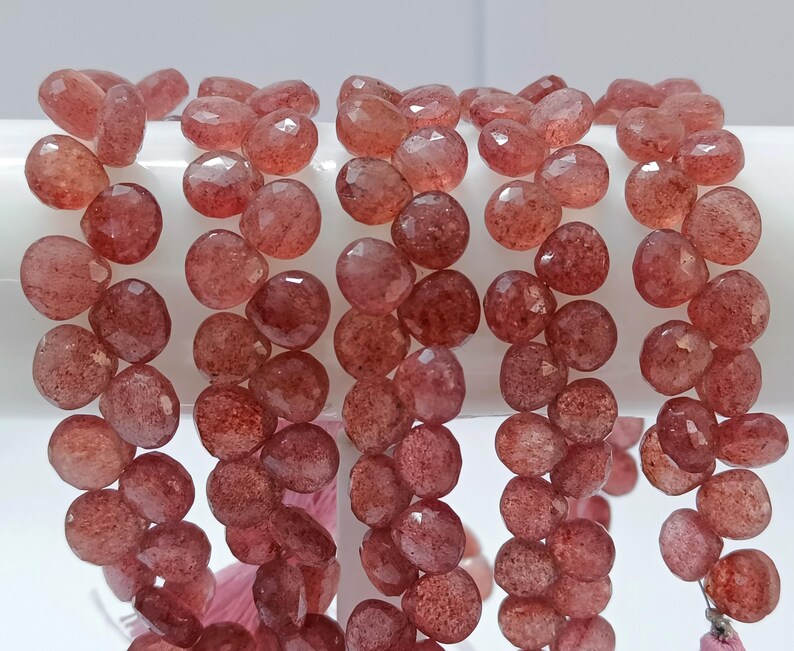May include: A strand of faceted, reddish-brown gemstone beads. The beads are round and have a slightly irregular shape. They are strung on a clear thread.