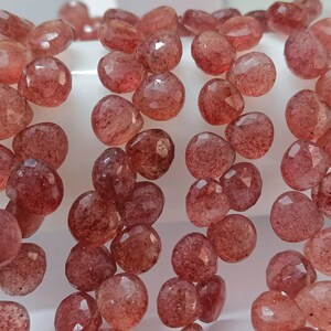 May include: A strand of red gemstone beads, each bead is faceted and has a slightly irregular shape. The beads are strung on a clear thread and are ready to be used for jewelry making.