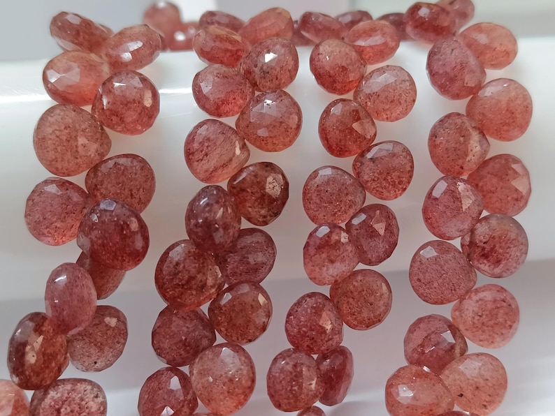 May include: A strand of red gemstone beads, each bead is faceted and has a slightly irregular shape. The beads are strung on a clear thread and are ready to be used for jewelry making.