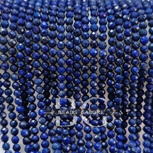 May include: A strand of deep blue faceted lapis lazuli beads. The beads are small and round, and they have a smooth, polished finish. "BEADS GALORE" is printed on a white banner.