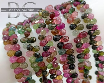 May include: A strand of multi-colored gemstone beads in a teardrop shape. The beads are a mix of pink, green, black, and brown.