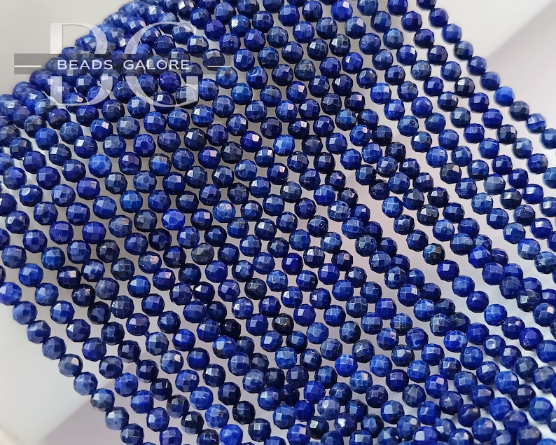 May include: A strand of deep blue lapis lazuli beads, each bead is faceted and has a round shape. The beads are strung together on a clear thread.