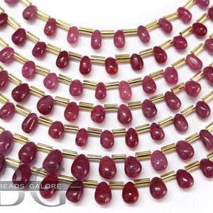 May include: A strand of ruby red gemstone beads, each bead is shaped like a teardrop and is separated by a gold spacer bead. The beads are strung on a gold thread.