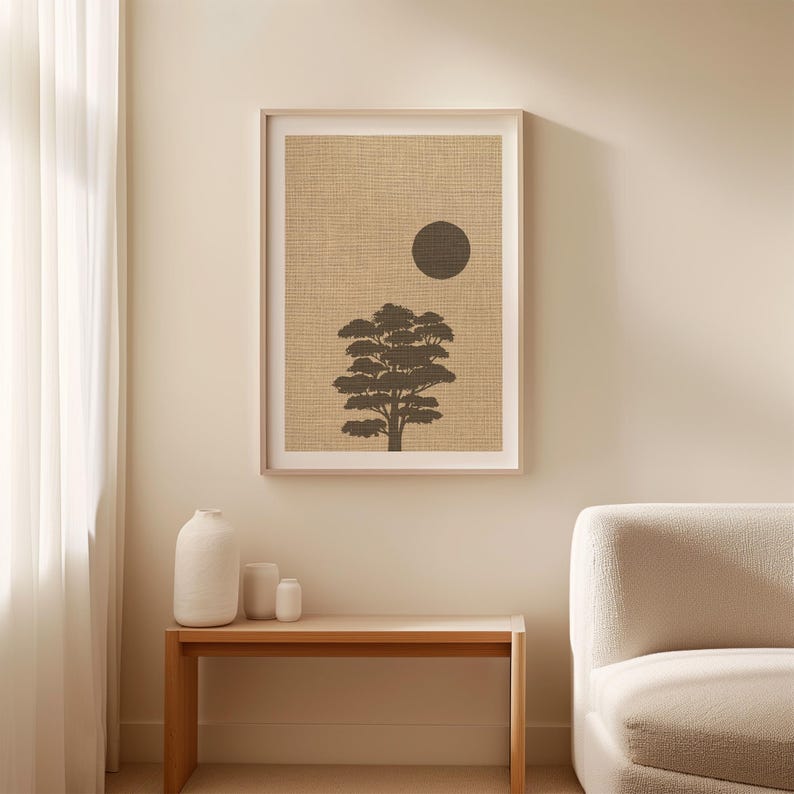 K&ouml;nnte beinhalten: Ein gerahmter Wandkunstdruck mit der dunkelbraunen Silhouette eines Baumes, zentriert unter einem massiven dunkelbraunen Kreis auf einem strukturierten beigen Hintergrund. Das Kunstwerk ist in einem hellen Rahmen und h&auml;ngt an einer Wand &uuml;ber einem Holztisch.