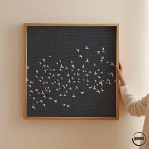 May include: A square wall art piece featuring a dark charcoal gray background with a textured linen-like appearance. Numerous small, white, stylized bird silhouettes are scattered across the surface in a flock formation. The print is encased in a light-toned wooden frame. The text SHIBUI PRINT STUDIO is visible in the bottom right corner.