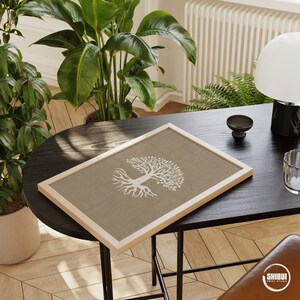 May include: A framed print of a white tree with roots on a brown linen background. The frame is light wood and the print is sitting on a black table.