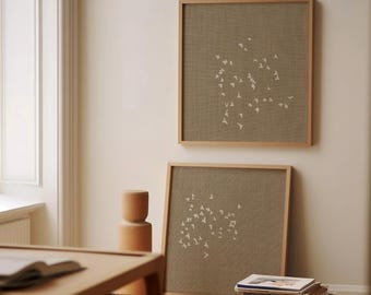 May include: Two square wall art pieces featuring light wood frames and textured taupe fabric backgrounds. Each piece displays a white screen-printed pattern of a flock of birds in flight, arranged in a scattered, organic formation across the centre.