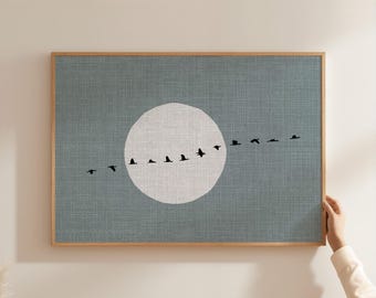 May include: A rectangular wall art print in a light wood frame featuring a textured blue-gray background with a large, solid white circle in the center. A horizontal line of small, black bird silhouettes flies across the white circle.