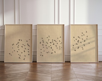 May include: A set of three rectangular wall art prints in light wooden frames. Each print features a beige textured background with a scattered pattern of small, dark brown silhouettes of birds in flight, arranged in unique groupings across each frame.