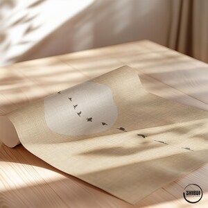 May include: A rolled-up beige yoga mat with a minimalist design featuring a white cloud shape and a flock of black birds in flight. The mat is on a wooden surface, with the logo "SHIBUI PRINT STUDIO" visible.