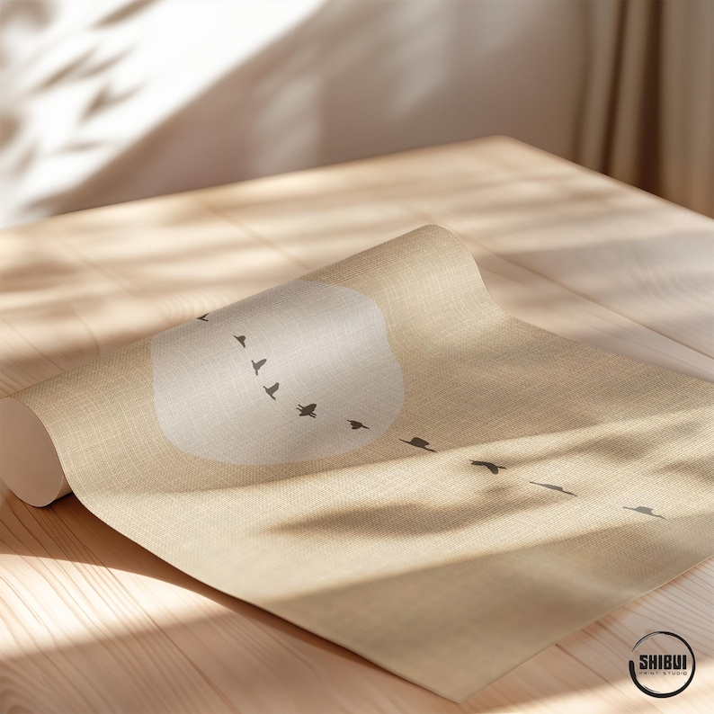May include: A rolled-up beige yoga mat with a minimalist design featuring a white cloud shape and a flock of black birds in flight. The mat is on a wooden surface, with the logo "SHIBUI PRINT STUDIO" visible.