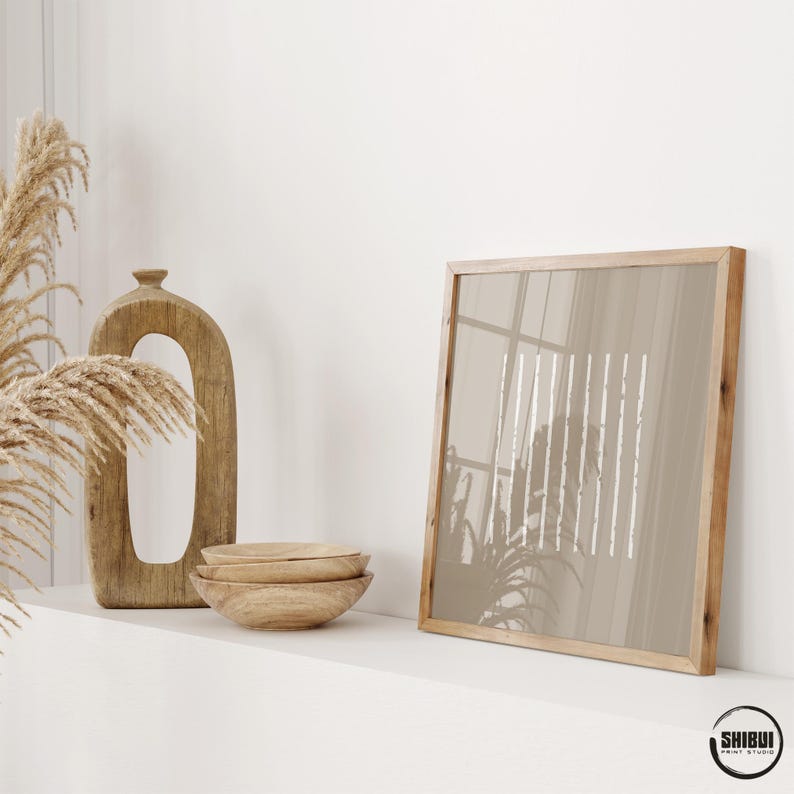 May include: A square wooden frame containing a print with vertical white lines on a beige background, a tall oval wooden sculpture, and a stack of three small wooden bowls. The text SHIBUI PRINT STUDIO is visible in the bottom right corner.