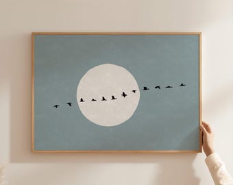 May include: A rectangular wall art print in a light wood frame featuring a muted blue background with a large, off-white circular moon shape in the center. A horizontal line of small, black bird silhouettes flies across the moon and sky.