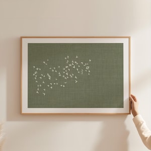 May include: A rectangular wall art piece featuring a textured olive green background with a white graphic pattern of a flock of birds in flight, enclosed within a light-toned wooden frame and bordered by a wide white matting.