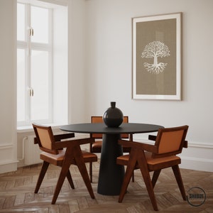 May include: A black round table with a black vase and four brown chairs with orange cushions. The table is set in a room with a white wall and a framed print of a white tree with roots on a brown background.