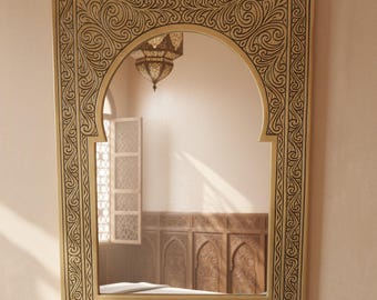 May include: A gold-coloured mirror with an arched top and an ornate black scrollwork frame. The mirror reflects a room with a window and decorative wall panels, creating a warm, inviting ambiance.