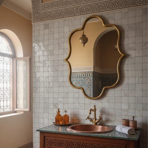 Puede incluir: Un espejo con marco dorado de forma ornamentada cuelga sobre un tocador de madera con un lavabo de cobre. El baño presenta azulejos estampados, un grifo de latón y botellas decorativas. Una pequeña linterna colgante se refleja en el espejo.
