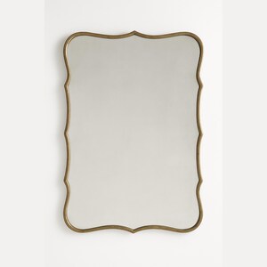 May include: A rectangular wall mirror with a decorative, scalloped gold-colored frame. The mirror's reflective surface is smooth and clear, reflecting the surrounding environment. The frame has an ornate, vintage-inspired design, adding a touch of elegance to any space.