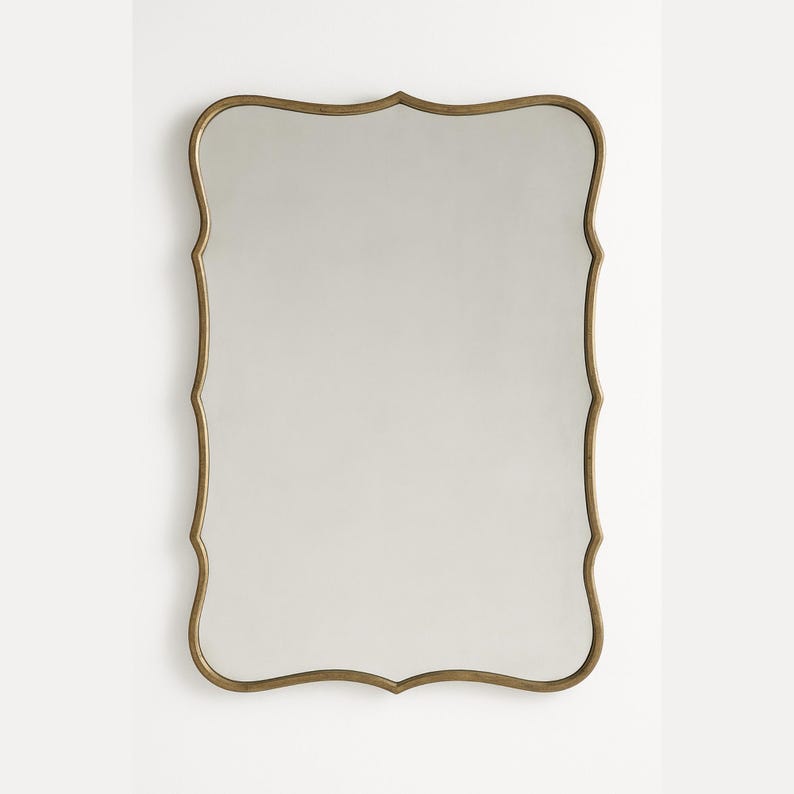 May include: A rectangular wall mirror with a decorative, scalloped gold-colored frame. The mirror's reflective surface is smooth and clear, reflecting the surrounding environment. The frame has an ornate, vintage-inspired design, adding a touch of elegance to any space.