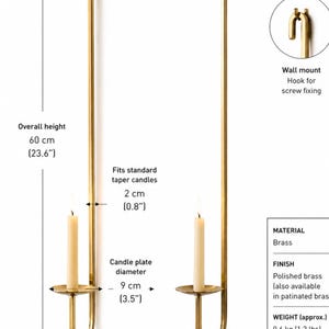 K&ouml;nnte beinhalten: Goldfarbene Wandleuchte mit geschwungenem Design, die eine brennende Kerze h&auml;lt. Die Gesamth&ouml;he betr&auml;gt 60 cm, die Breite 10 cm und der Abstand zur Wand 13 cm. Aus poliertem Messing.