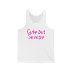 Könnte beinhalten: Weißes Tanktop mit dem Text "Cute but Savage" in rosa, blasenartigen Buchstaben. Das ärmellose Oberteil hat einen Rundhalsausschnitt und besteht aus einem weichen, leichten Material. Ein lässiges und bequemes Kleidungsstück.
