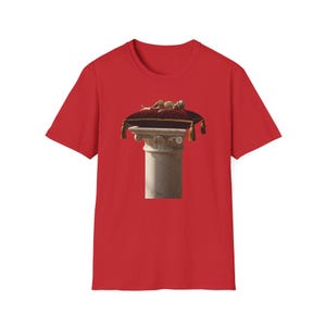 Könnte beinhalten: Rotes T-Shirt mit einer Grafik eines Skeletts auf einem roten Samtkissen auf einer Marmorsäule. Das Kissen hat goldene Quasten. Das Design ist mittig auf der Vorderseite des Shirts angeordnet.