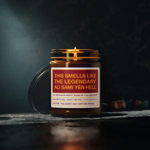 Peut inclure: Une bougie en pot de verre brun avec une mèche allumée et une étiquette blanche portant le texte rouge : THIS SMELLS LIKE THE LEGENDARY ALI SAMI YEN HELL, FULL-SIZE STADIUM ENERGY, MADE OF %100 LION HEART, WELCOME TO HELL - ENJOY THE FIRE, CAUTION: THIS SCENT MAY DISTURB RIVALS.