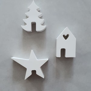 Könnte beinhalten: Drei weiße Holzornamente: ein Weihnachtsbaum, ein Haus mit einem Herz-Ausschnitt und ein Stern. Die Ornamente sind schlicht und modern, perfekt zum Dekorieren eines Hauses für die Feiertage.