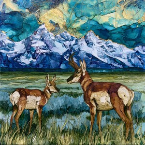 May include: A square art print featuring two pronghorn antelopes standing in a grassy field. The background displays jagged, snow-capped mountains under a swirling, abstract sky of deep blue, teal, and gold ink-wash textures and patterns.