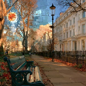 May include: A dark green metal park bench sits on a stone path beside a black iron fence and a tall street lamp. The scene features white multi-story buildings and trees with autumn leaves, overlaid with a circular, mosaic-style glass pattern.