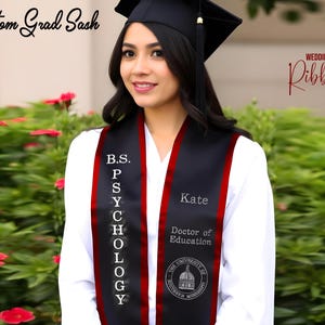 May include: A black graduation sash with red trim. The sash has the text "B.S. PSYCHOLOGY" on one side and "Kate Doctor of Education" on the other side. The sash also has a small logo of the University of Southern Mississippi.