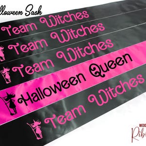 Könnte beinhalten: Schwarzer und rosa Halloween-Schärpe mit dem Text "Halloween Sash" und "Team Witches", der auf jedem der fünf Streifen wiederholt wird. Die Schärpe hat auch eine Silhouette einer Hexe auf jedem Streifen.