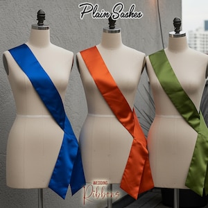May include: Three satin sashes in blue, orange, and green are displayed on dress forms. The sashes are draped diagonally across the forms. The text "Plain Sashes" is at the top, and "Wedding Ribbons" is at the bottom.