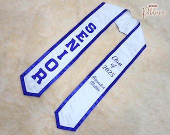 May include: White graduation sash with blue trim and the text "Class of 2025" and "Branddon Balda" embroidered in blue.