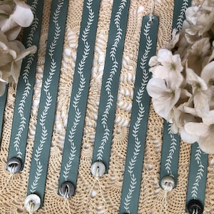 May include: Set of six blue ribbon bookmarks with white leaf designs and white buttons. The bookmarks are arranged on a crocheted doily.