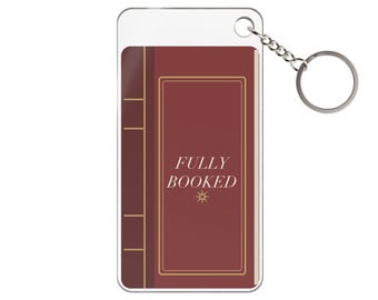 May include: A rectangular acrylic keyring featuring a maroon book design with gold-coloured border lines and the text "FULLY BOOKED" printed in white, accompanied by a small star icon and a silver-toned metal split ring attachment.