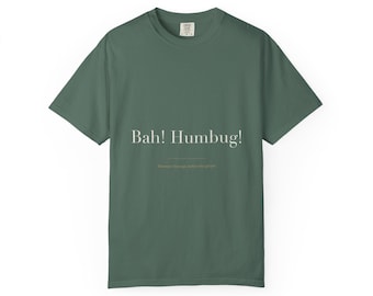 May include: A dark sage green short-sleeve t-shirt featuring the white text Bah! Humbug! printed in a serif font across the chest. A thin horizontal line is positioned below the text, followed by smaller, less legible text underneath.
