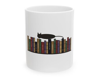 May include: A white ceramic mug featuring a graphic of a black cat silhouette resting on top of a row of colourful book spines. The books include titles such as Moby Dick, Walden, Hard Times, The Odyssey, and Candide, arranged on a shelf.