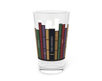 May include: A clear glass pint glass featuring a colourful graphic print of a row of books. The spines are coloured in green, red, purple, and tan. The text on the book spines includes the words Walden, Emma, The Odyssey, and Kim.