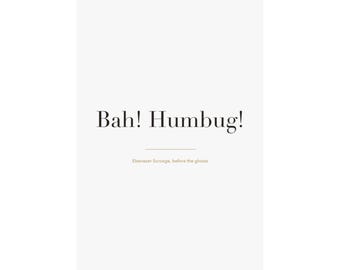 May include: A white vertical poster hanging from two black clips. The text "Bah! Humbug!" is printed in large black serif font in the centre. Below this, a thin horizontal line and the smaller text "Ebenezer Scrooge, before the ghosts".