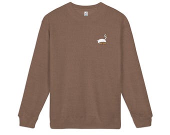 May include: A brown crewneck sweatshirt featuring a small embroidered graphic on the left chest. The graphic depicts a white goose wearing brown glasses and sitting inside a brown cardboard box, with a white label visible at the neckline.