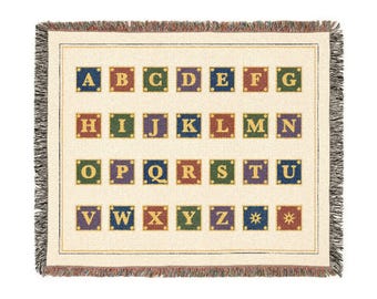 May include: A cream-coloured woven throw blanket featuring a grid of colourful squares, each containing a gold letter of the alphabet from A to Z. The blanket has a fringed edge and includes two additional squares with gold star symbols.