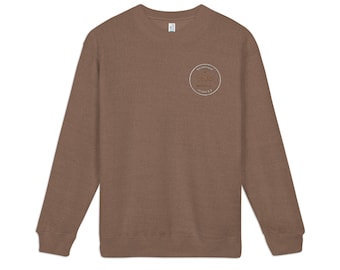 May include: A brown long-sleeve crewneck sweatshirt featuring a circular embroidered patch on the left chest. The patch contains the text "SUMMER OF 1976" in a circular arrangement with a central graphic element, all stitched in a light thread.