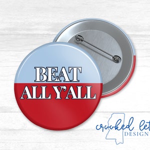 May include: A red and blue button with the text "BEAT ALL Y'ALL" in white. The button is a promotional item for a sports team or event.
